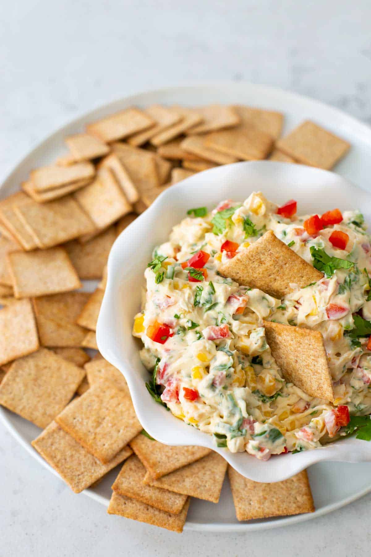 A serving of poolside dip has wheat crackers dunking a scoop.