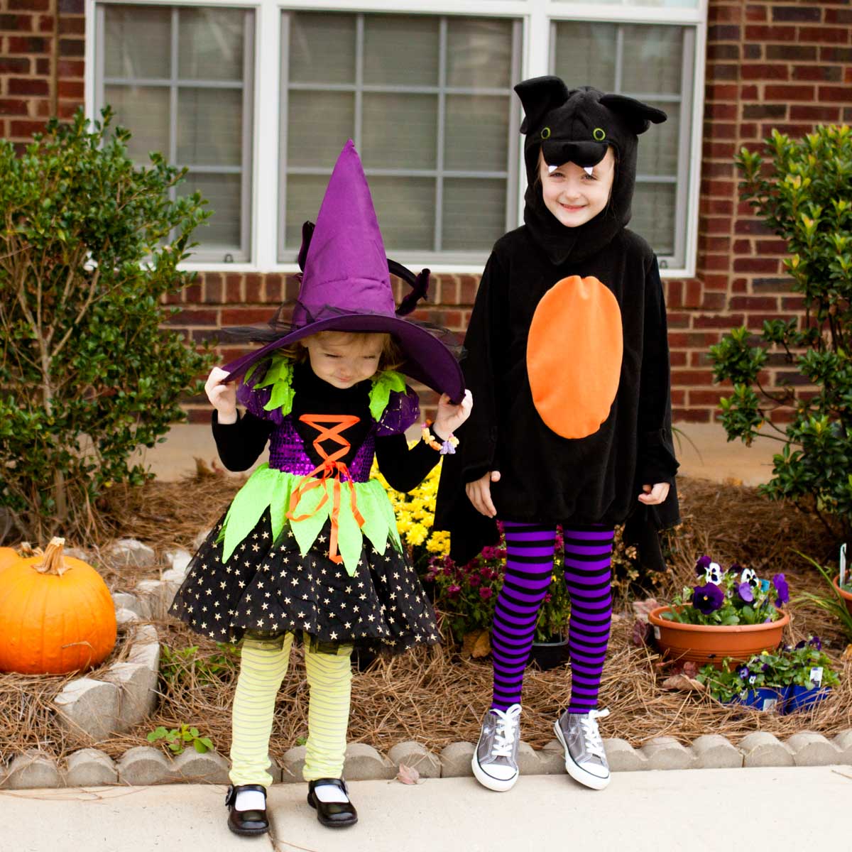 Two preschoolers in their Halloween costumes stand in front of their house.