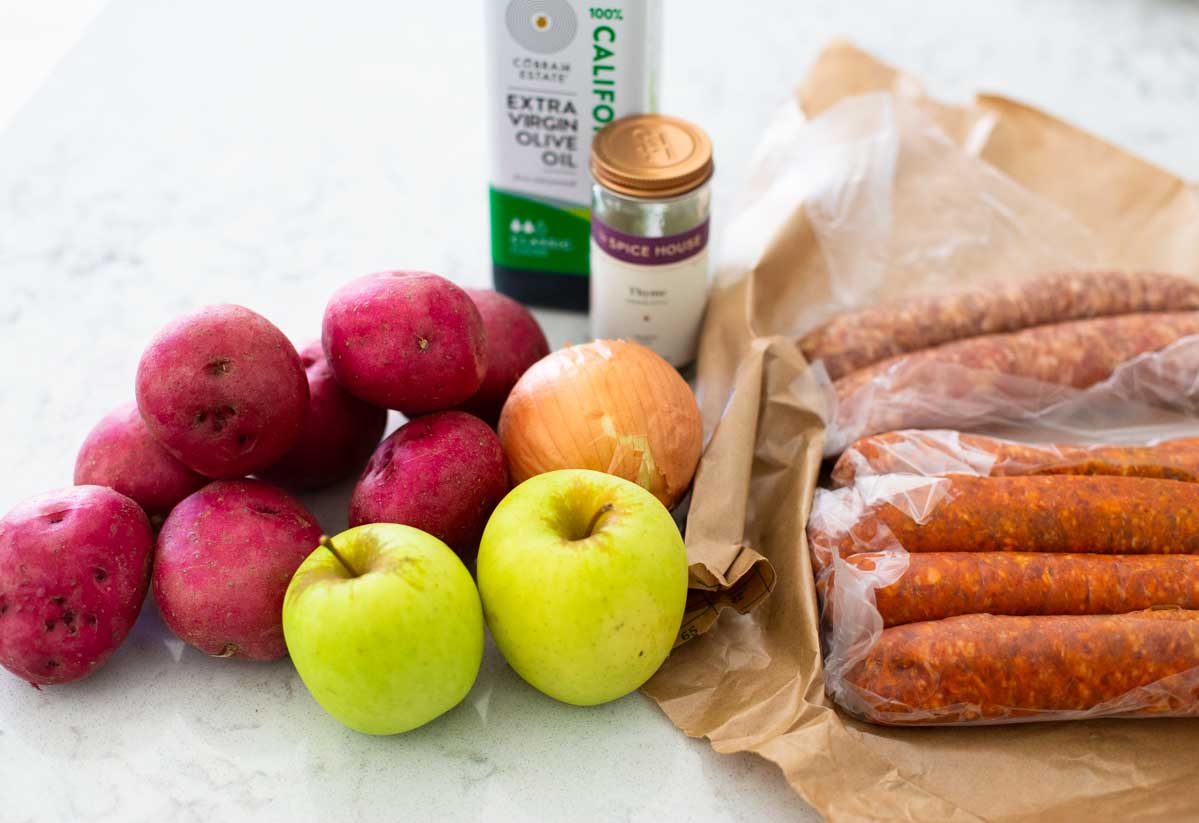 The ingredients for roasted sausages, apples, and potatoes are on the kitchen counter.