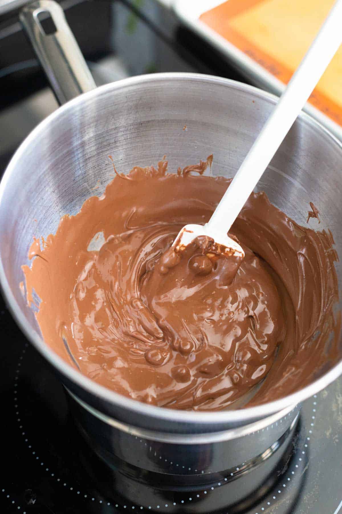 The chocolate chips have melted and a white spatula is stirring them.