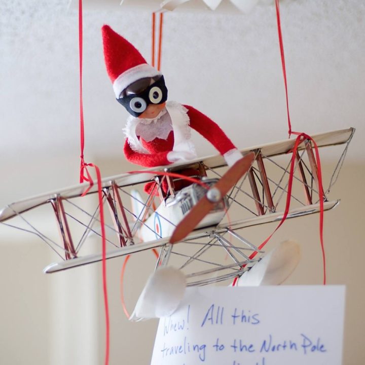An Elf on the Shelf is flying in a toy airplane.