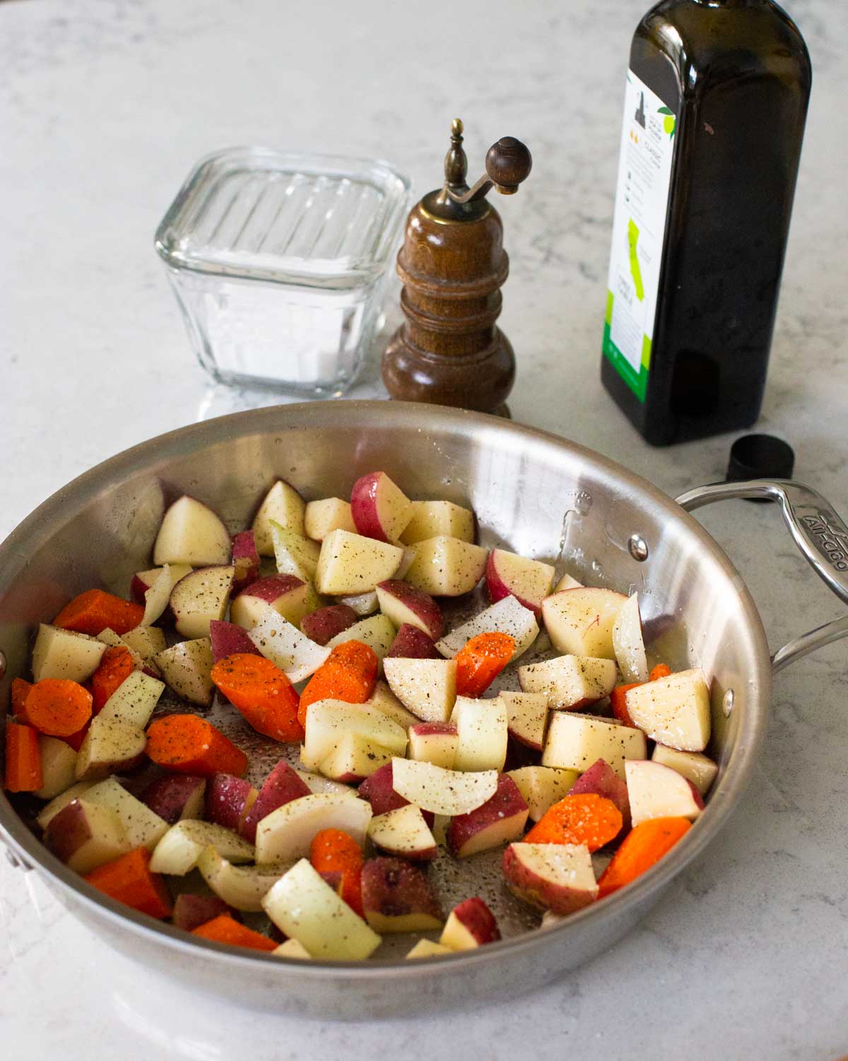 The potatoes, carrots, and onions have been chopped and tossed with olive oil in a large round roasting pan.
