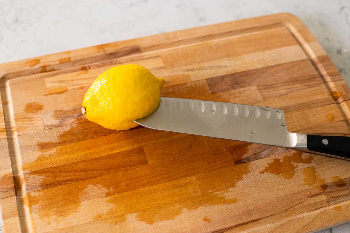 A knife is piercing a fresh lemon before it is inserted in the chicken.