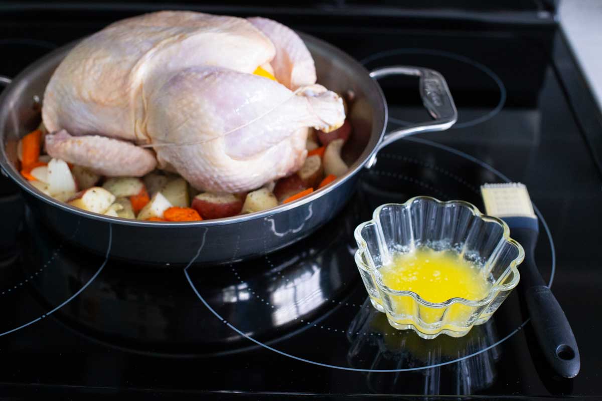 The chicken has been added to the pan and a bowl of melted butter with a pastry brush is ready for topping