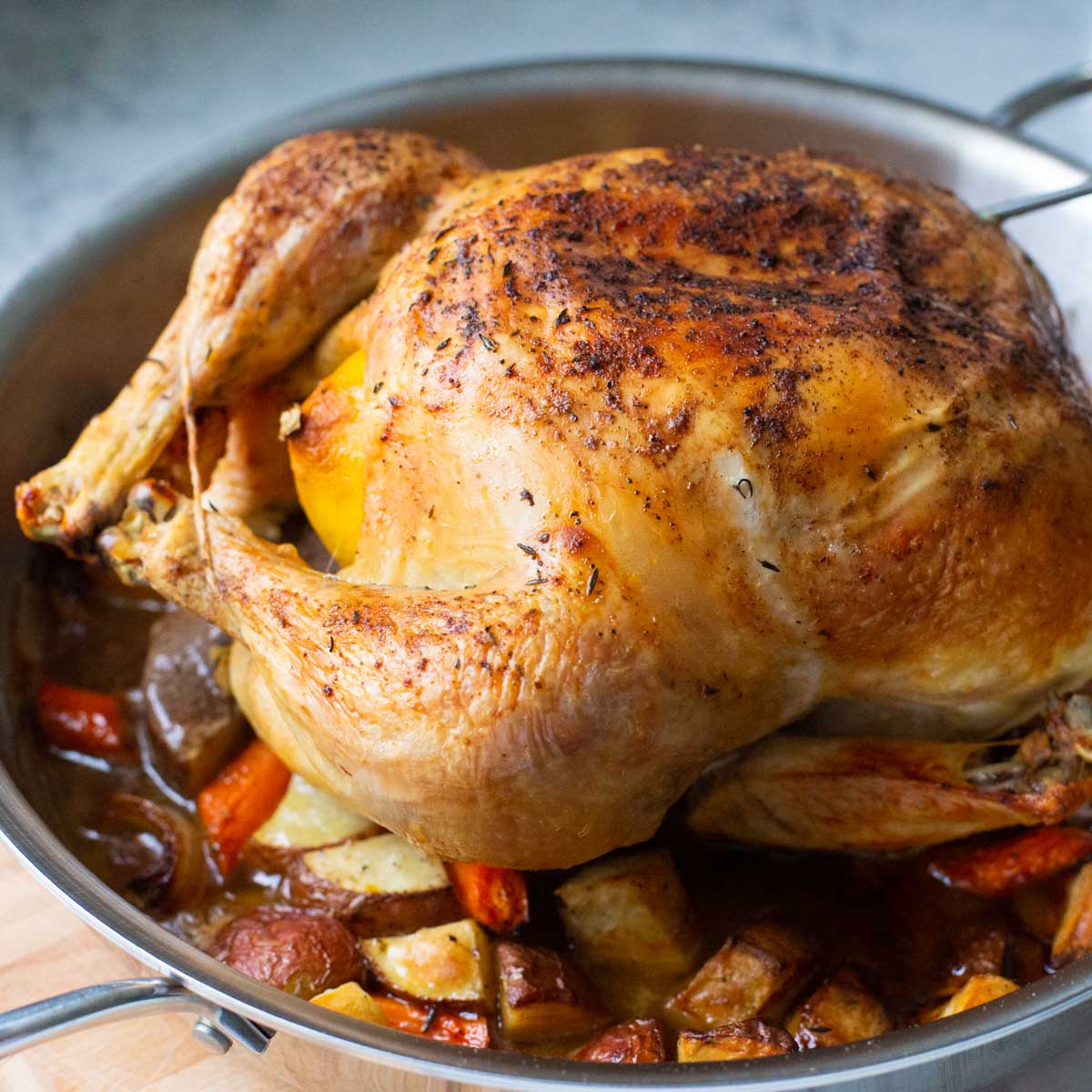 The roasted chicken sits on top of roasted vegetables in a round roasting pan.