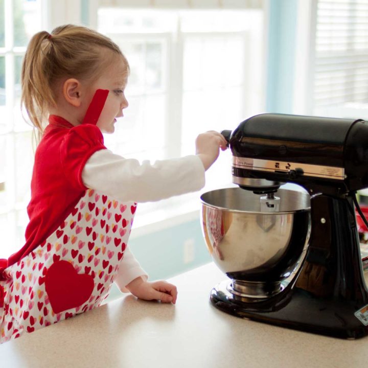 A little girl helps to operate the kitchen stand mixer while baking with parents.