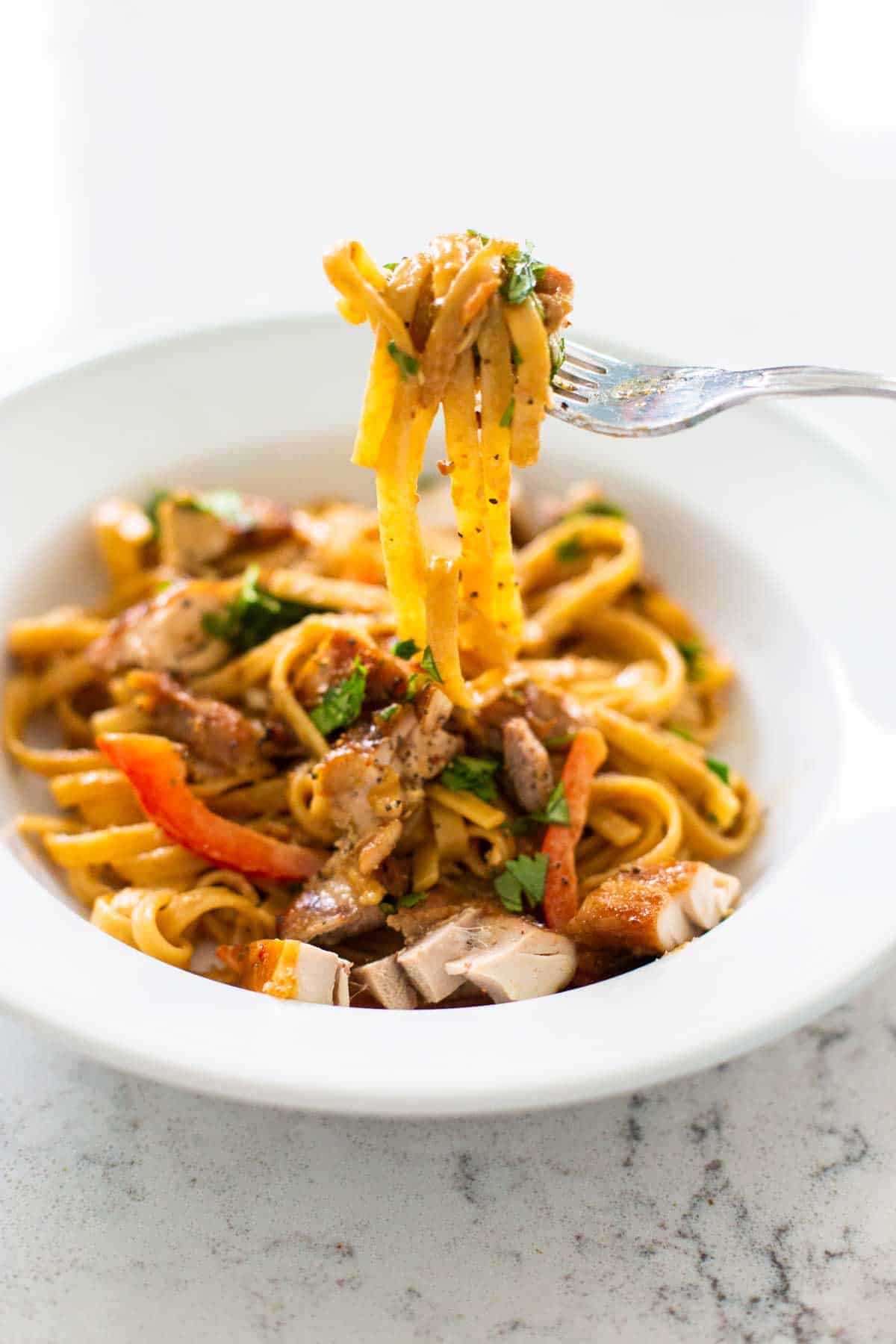 A bowl of peanut butter noodles has a fork pulling up the pasta to show the sauce and veggies.