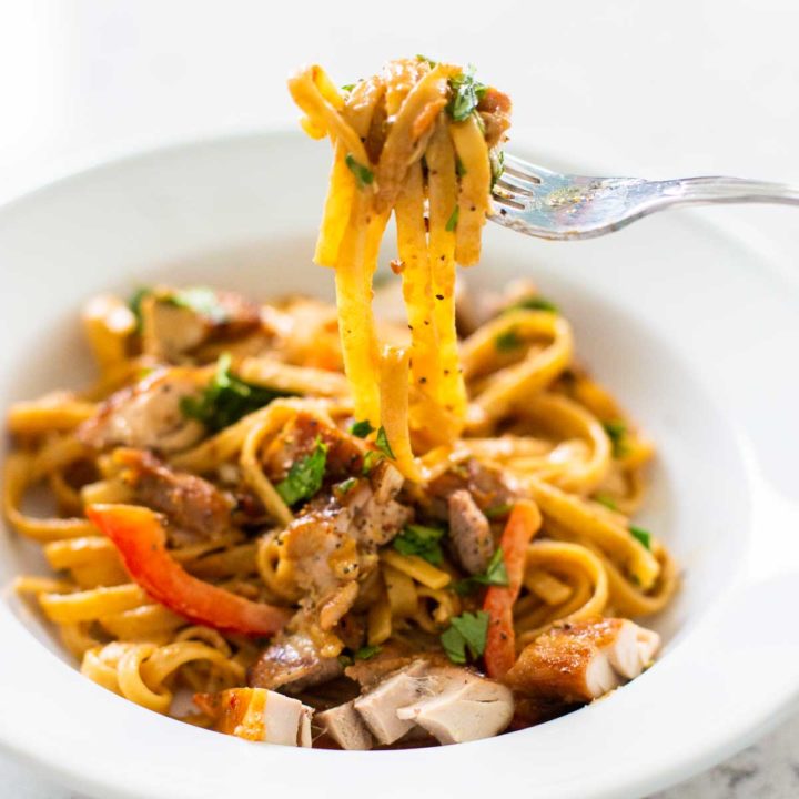 A bowl of peanut butter noodles has a fork pulling up the pasta to show the sauce and veggies.