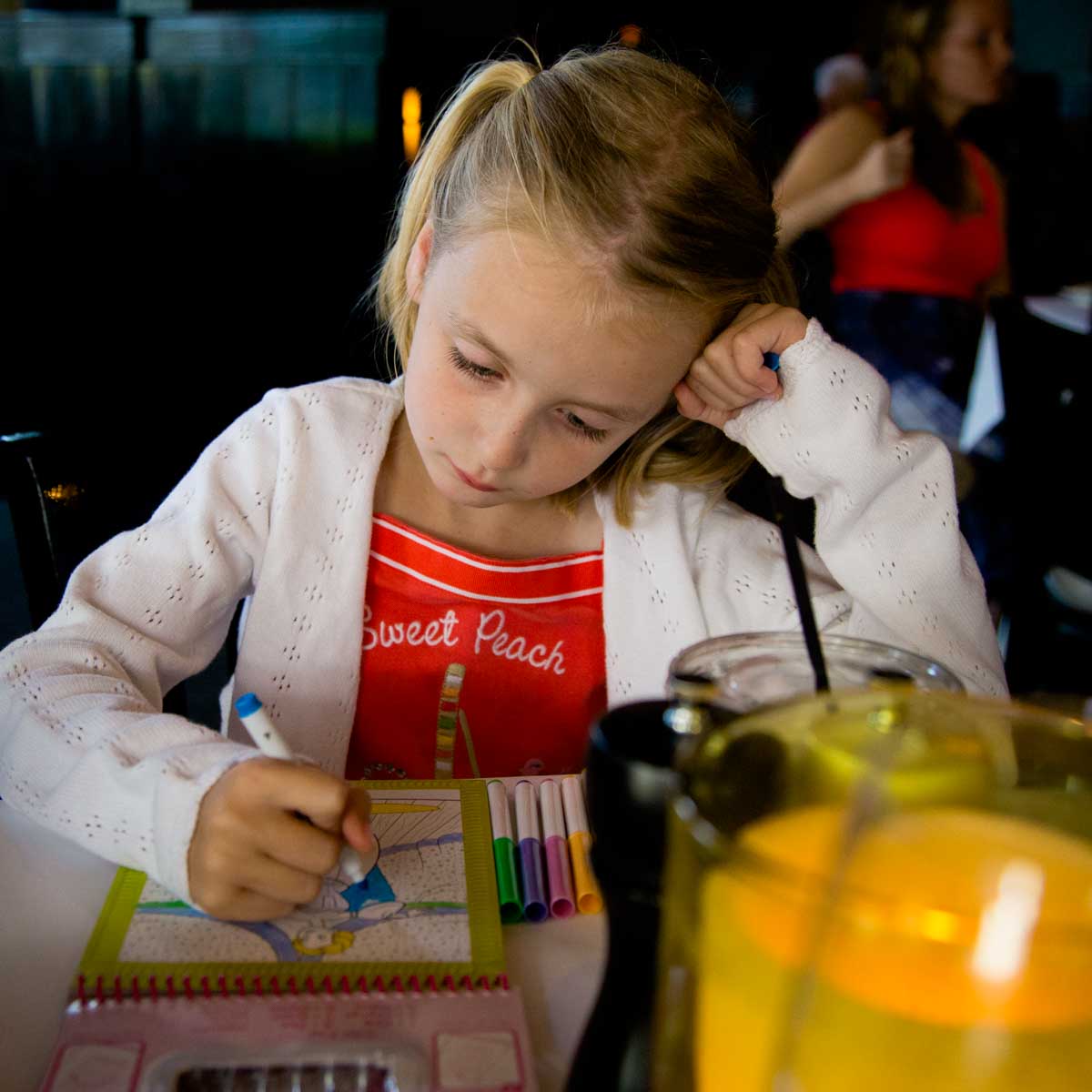 A young girl colors at a restaurant table.