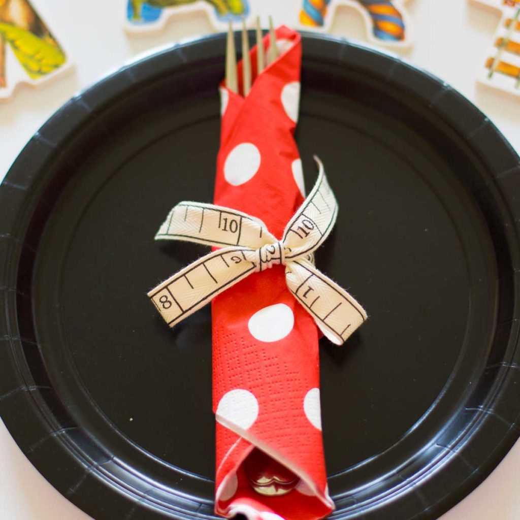 A black paper plate with utensils rolled up in a red and white polka dot napkin.