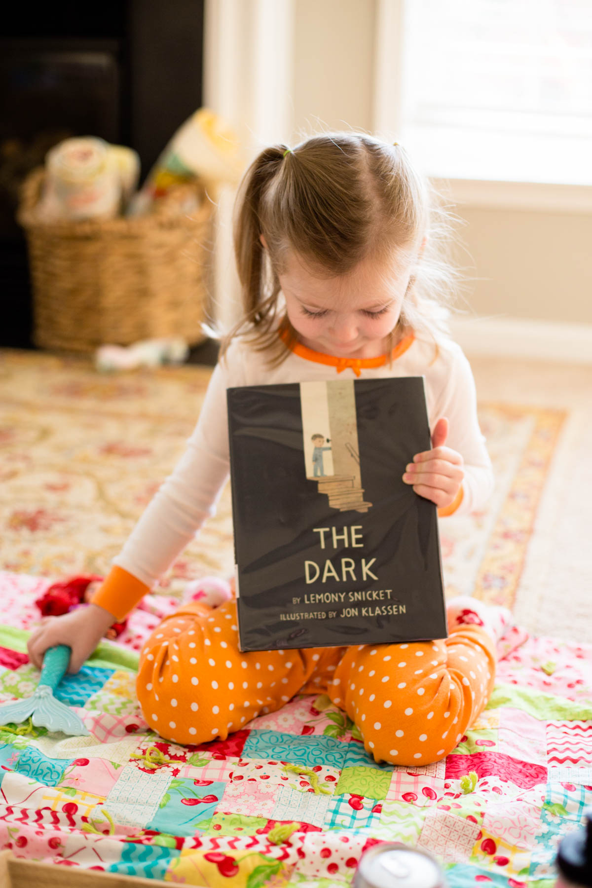 A young girl holds a fall picture book on the floor in the living room.