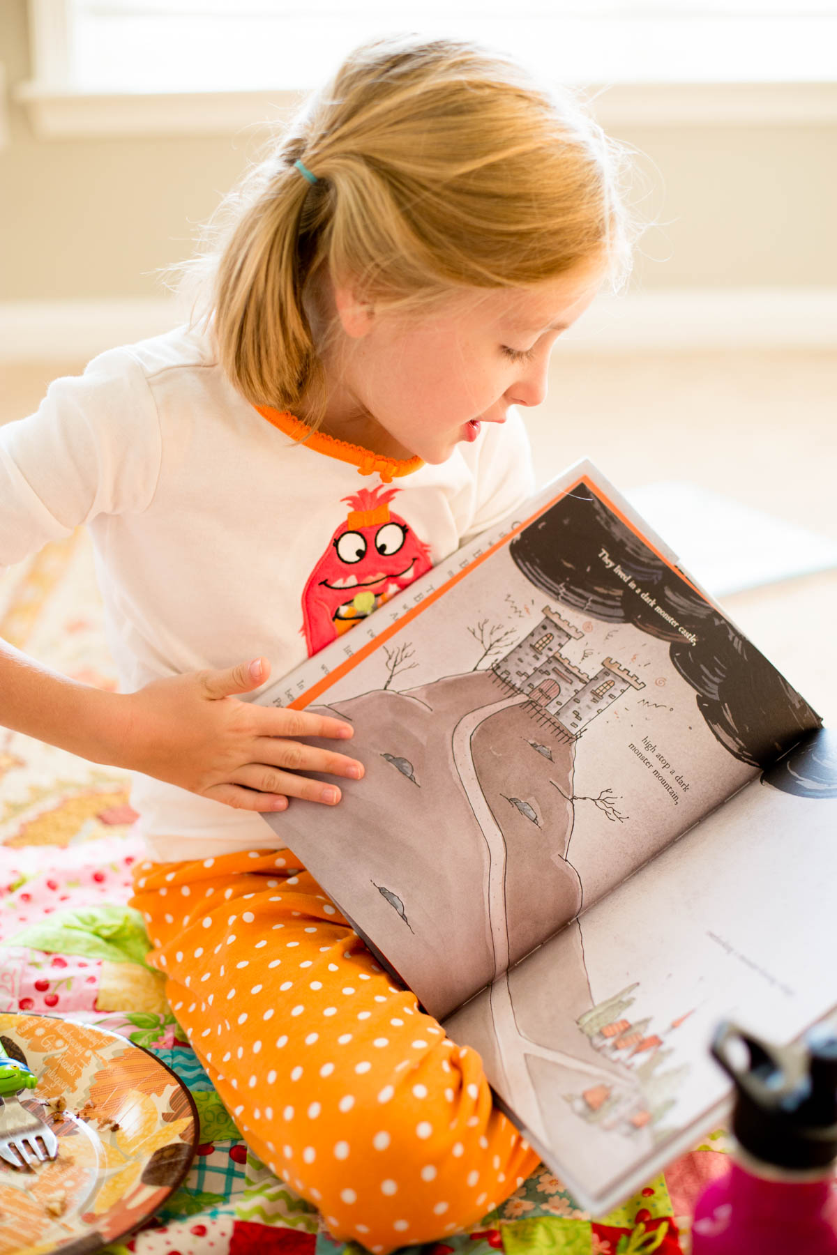 A girl reads out loud from a Halloween picture book while sitting on the living room floor.