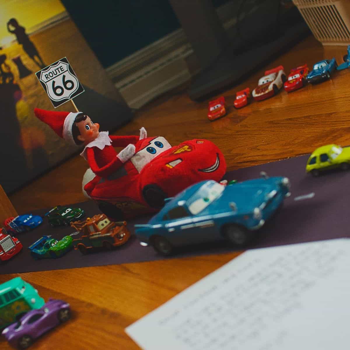 An Elf on the Shelf rides a toy car racetrack.