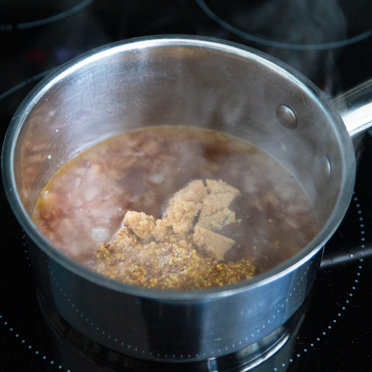 The brown sugar and mustard are cooking together in a saucepan on the stovetop.