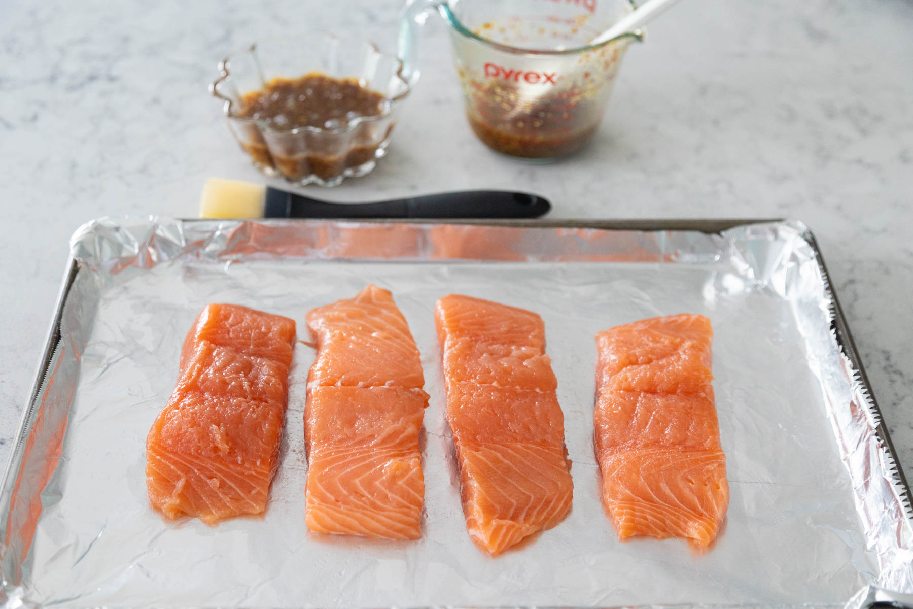 The four salmon filets are lined up on a baking pan ready to be glazed.