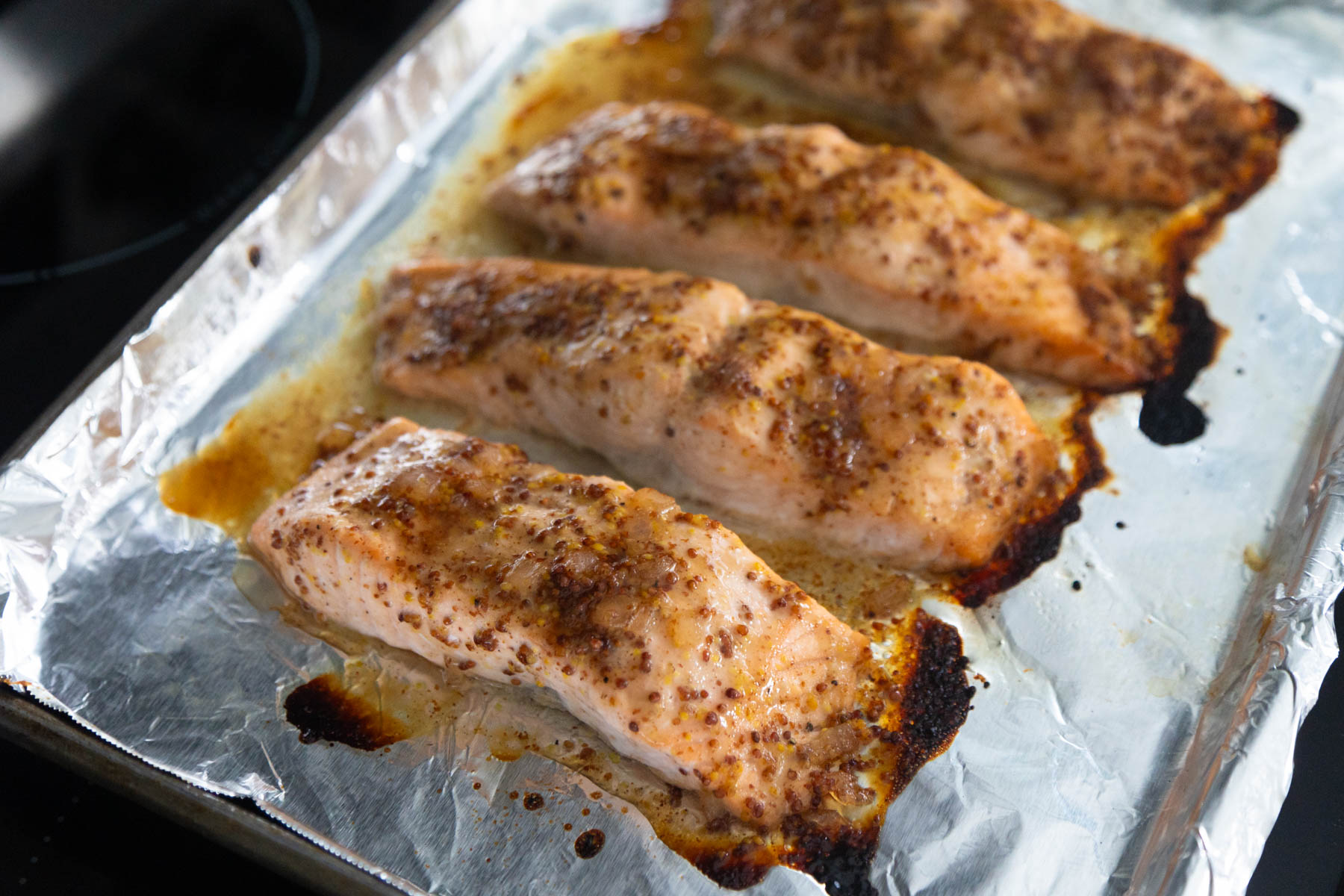 The broiled salmon filets are cooling on the stovetop. They have a golden brown edge.