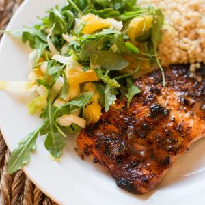 A plate with mustard glazed salmon and a leafy citrus salad with a scoop of couscous side dish.