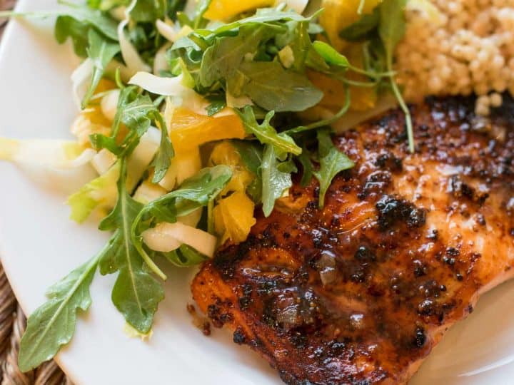 A plate with mustard glazed salmon and a leafy citrus salad with a scoop of couscous side dish.