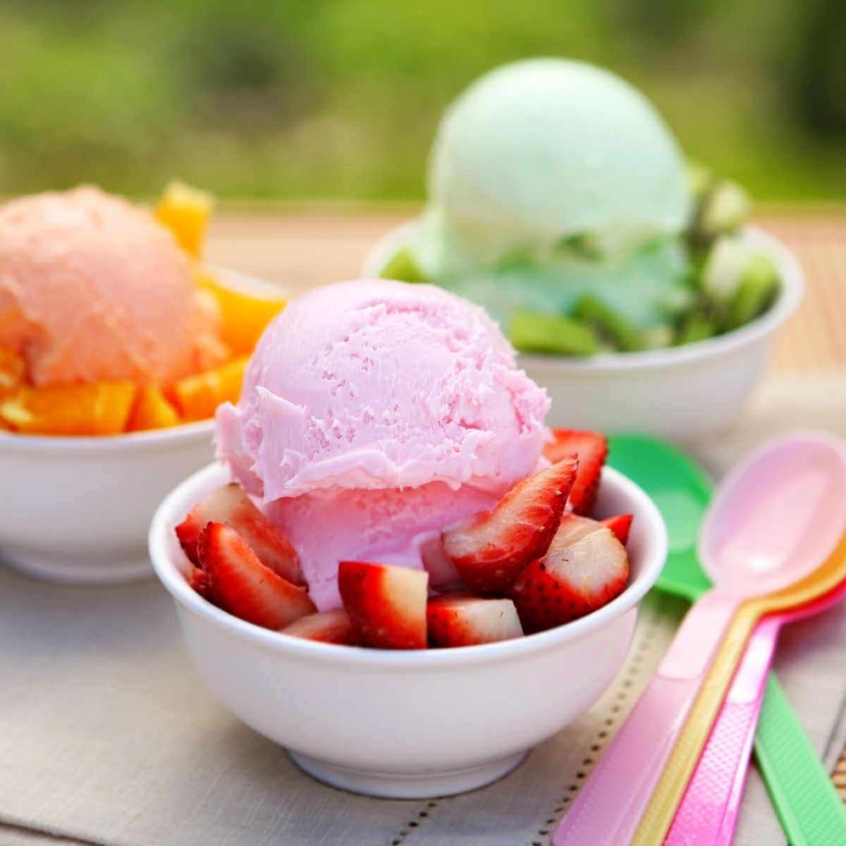 Bowls of ice cream with fresh fruit and colorful spoons.
