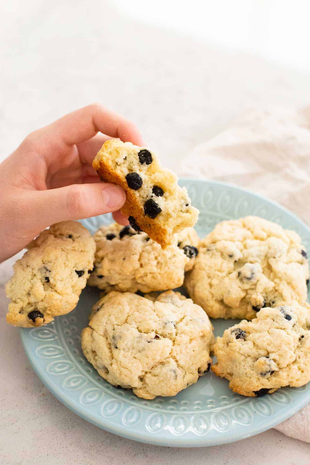 A young child's hand is holding a broken scone half to show the inside texture.