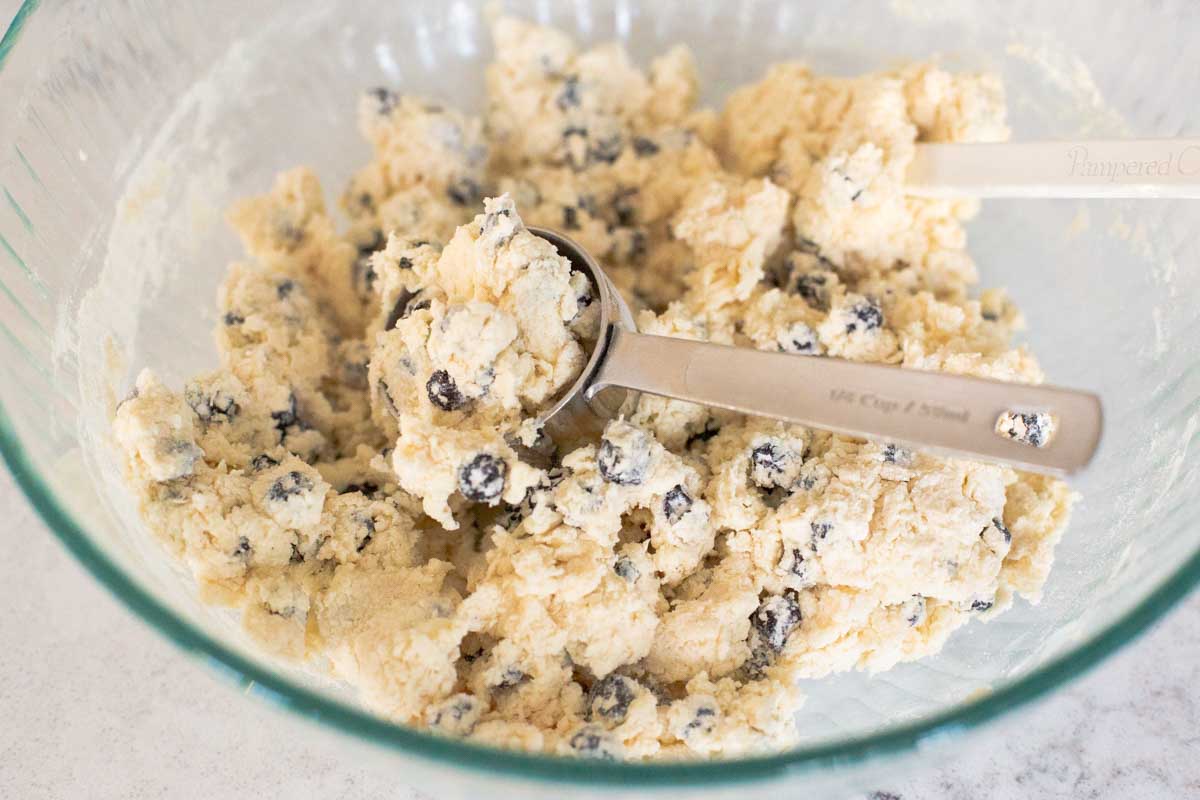 The scone dough has been mixed together and a 1/4 cup measuring cup is used as a scoop to portion the scones.