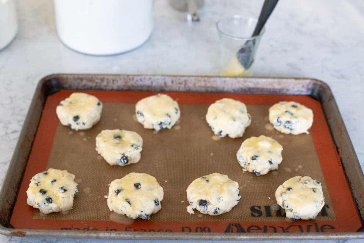 The baking pan of scones has melted butter being brushed over the top.