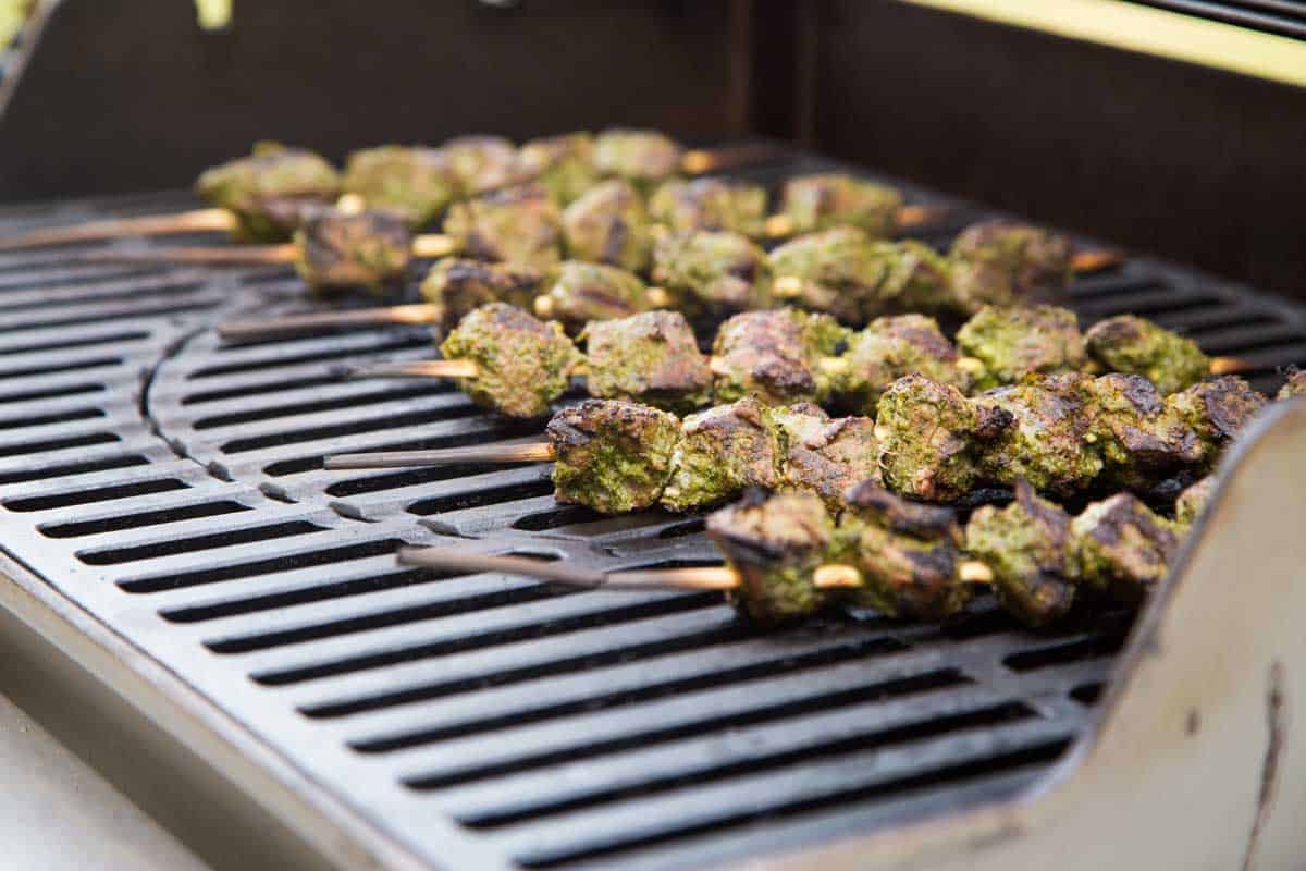 The kabobs of beef chunks are cooking on the grill.