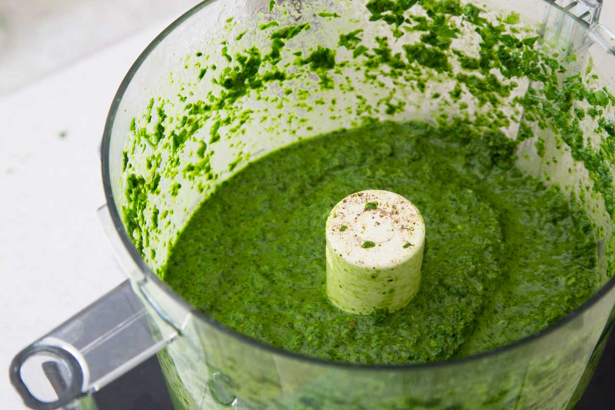 The finished green chimichurri sauce is smooth and blended in the food processor bowl.