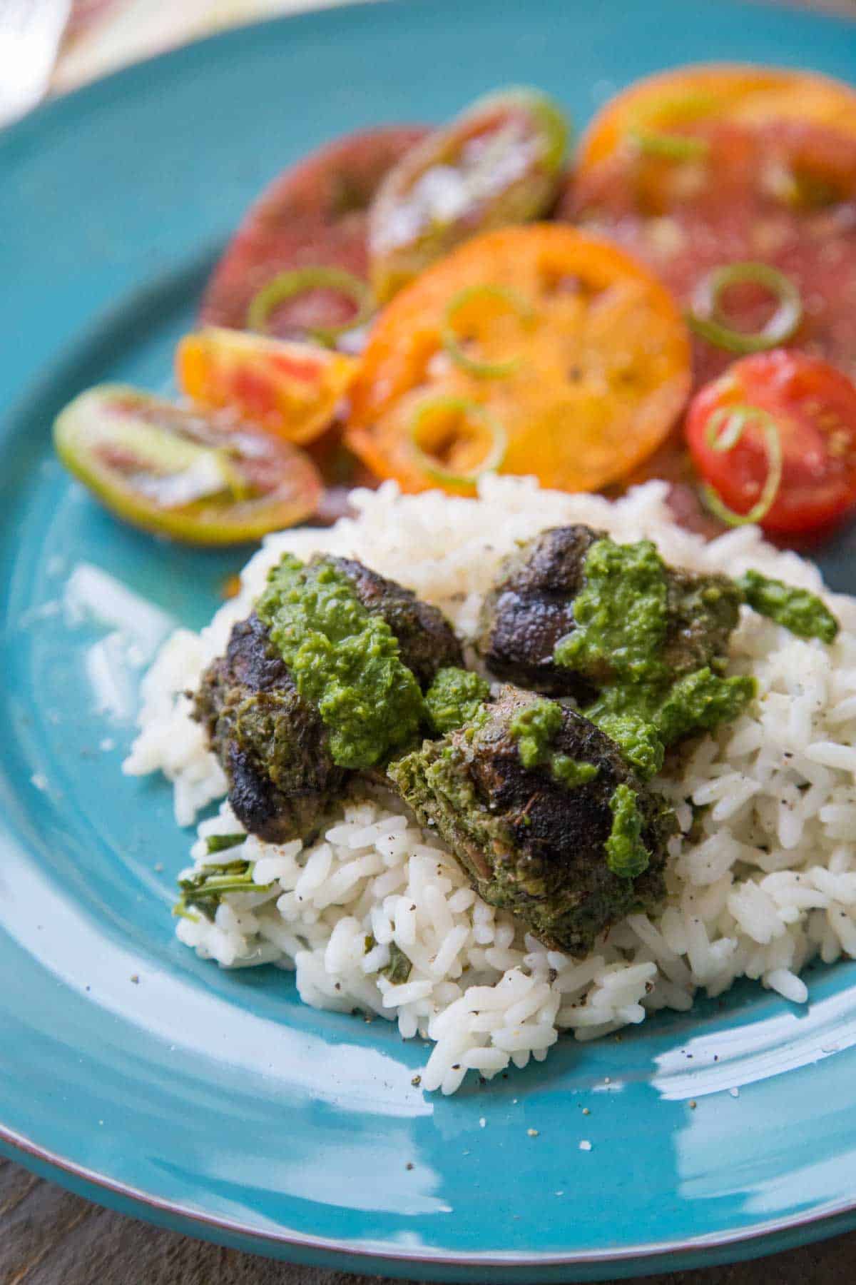 The finished steak is on a bed of rice with green chimichurri sauce drizzled over the top. Fresh tomatoes are in the background.