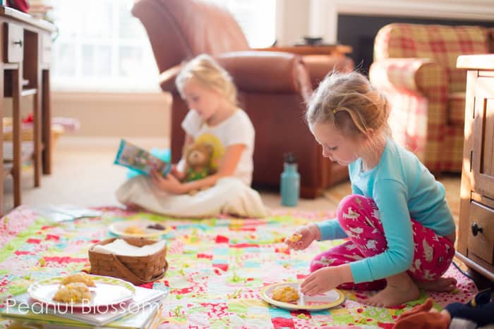 Two young girls eating scones during a breakfast picnic on the living room floor.