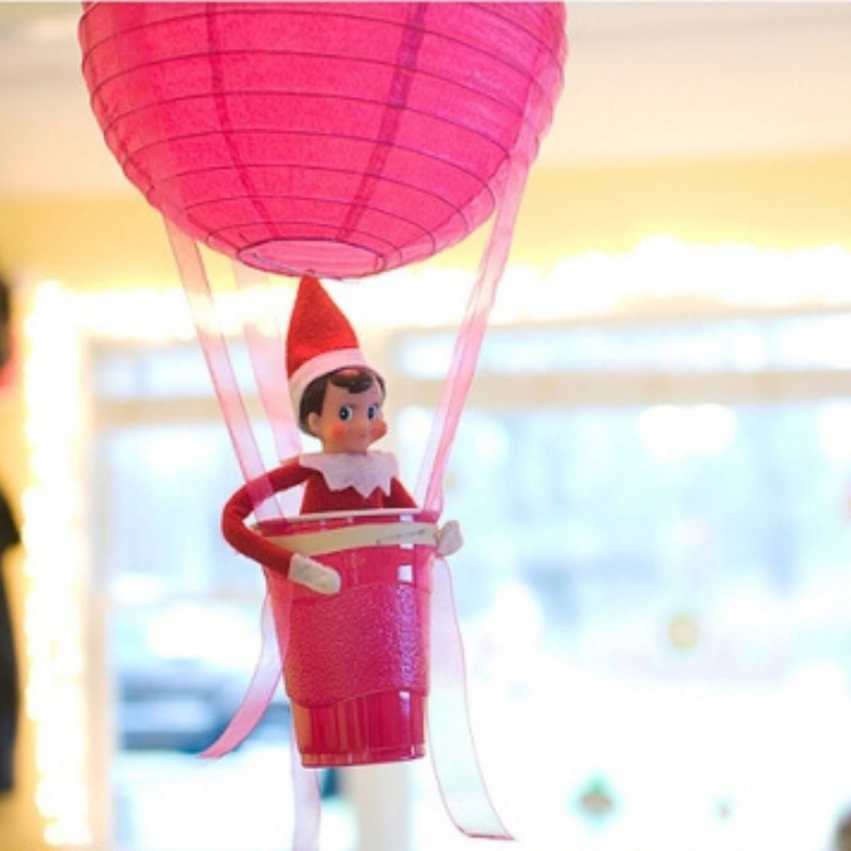 The Elf on the Shelf is sitting in a homemade 'hot air balloon' made from a red plastic cup and a streamer.