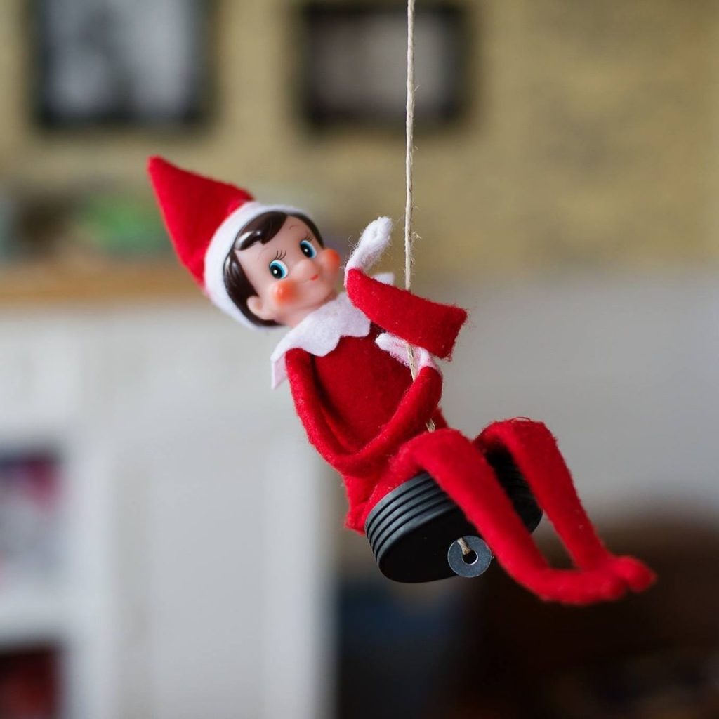 The Elf on the Shelf is swinging on a homemade swing in the living room.