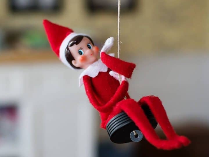 The Elf on the Shelf is swinging on a homemade swing in the living room.