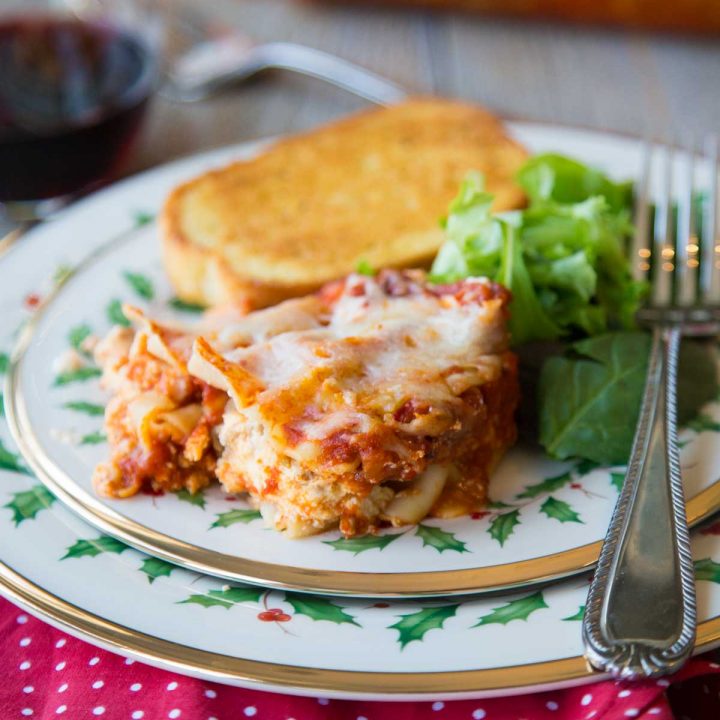 A slice of lasagna sits on a festive holiday plate with a green salad and slice of garlic bread.