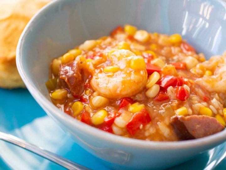 A blue bowl of spicy shrimp stew shows tons of corn, red peppers, spicy sausage, and big shrimp.