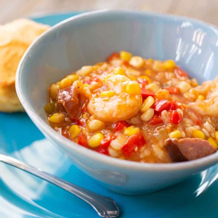 A blue bowl of spicy shrimp stew shows tons of corn, red peppers, spicy sausage, and big shrimp.