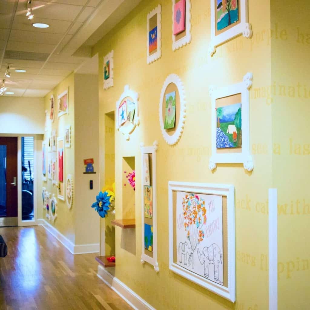 A yellow painted hallway with white trim displays framed children's artwork.