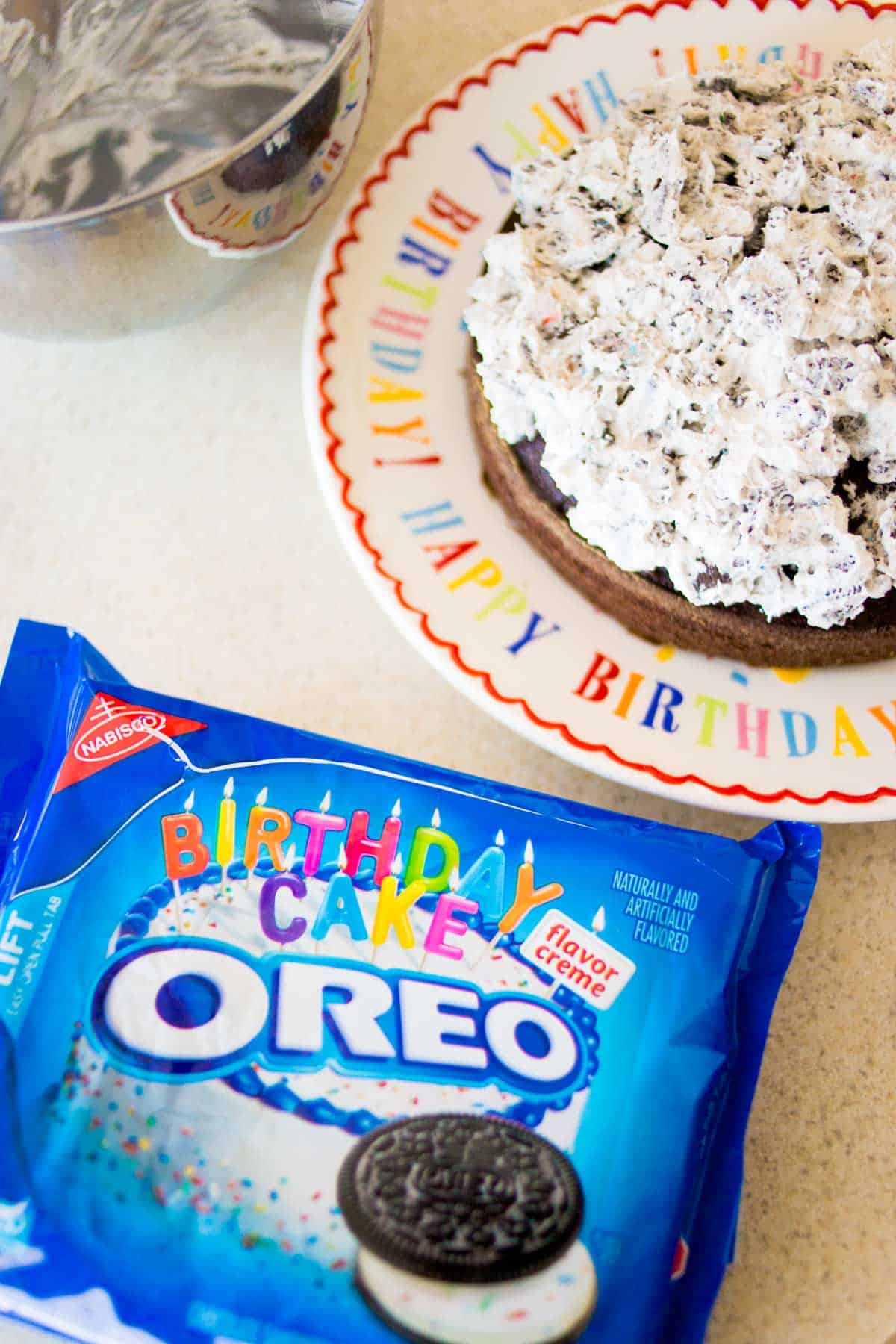 A package of OREO cookies on the counter next to a birthday cake being assembled.