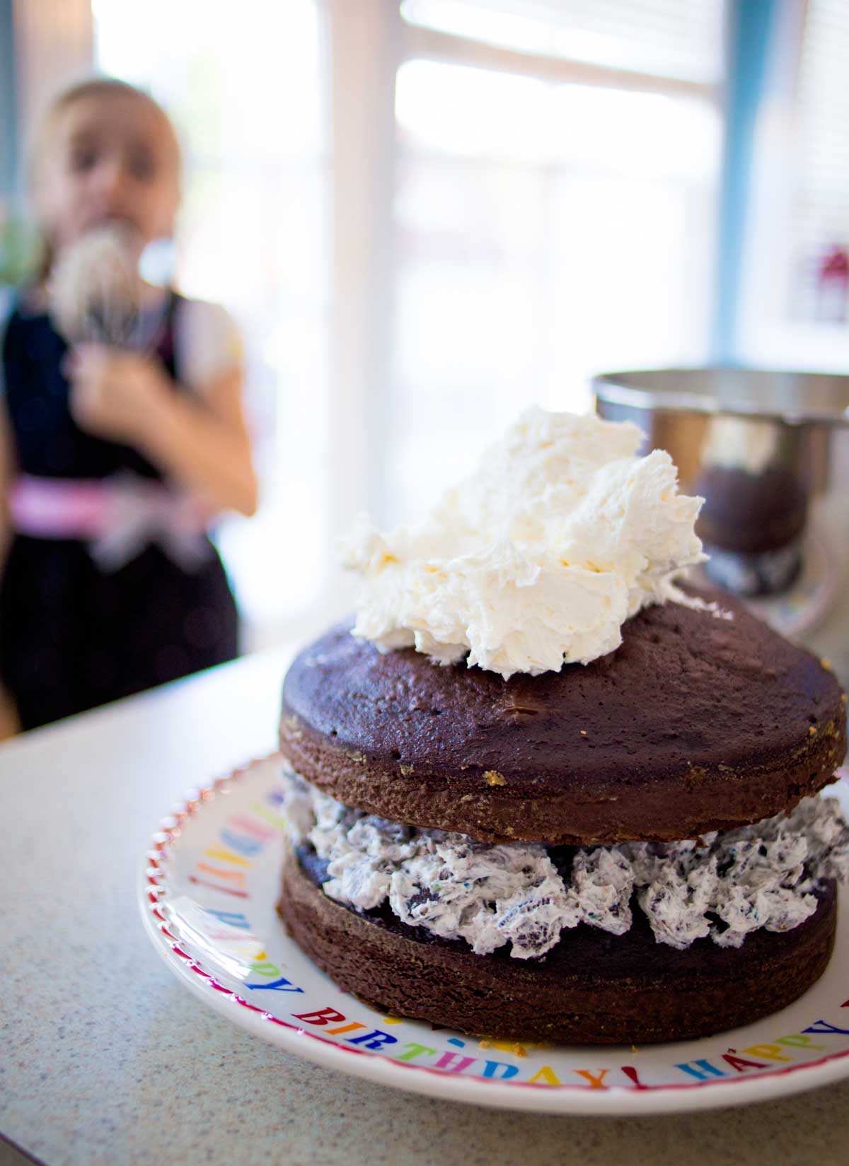 The chocolate cake has been stacked with a dollop of frosting on top about to be spread over it.