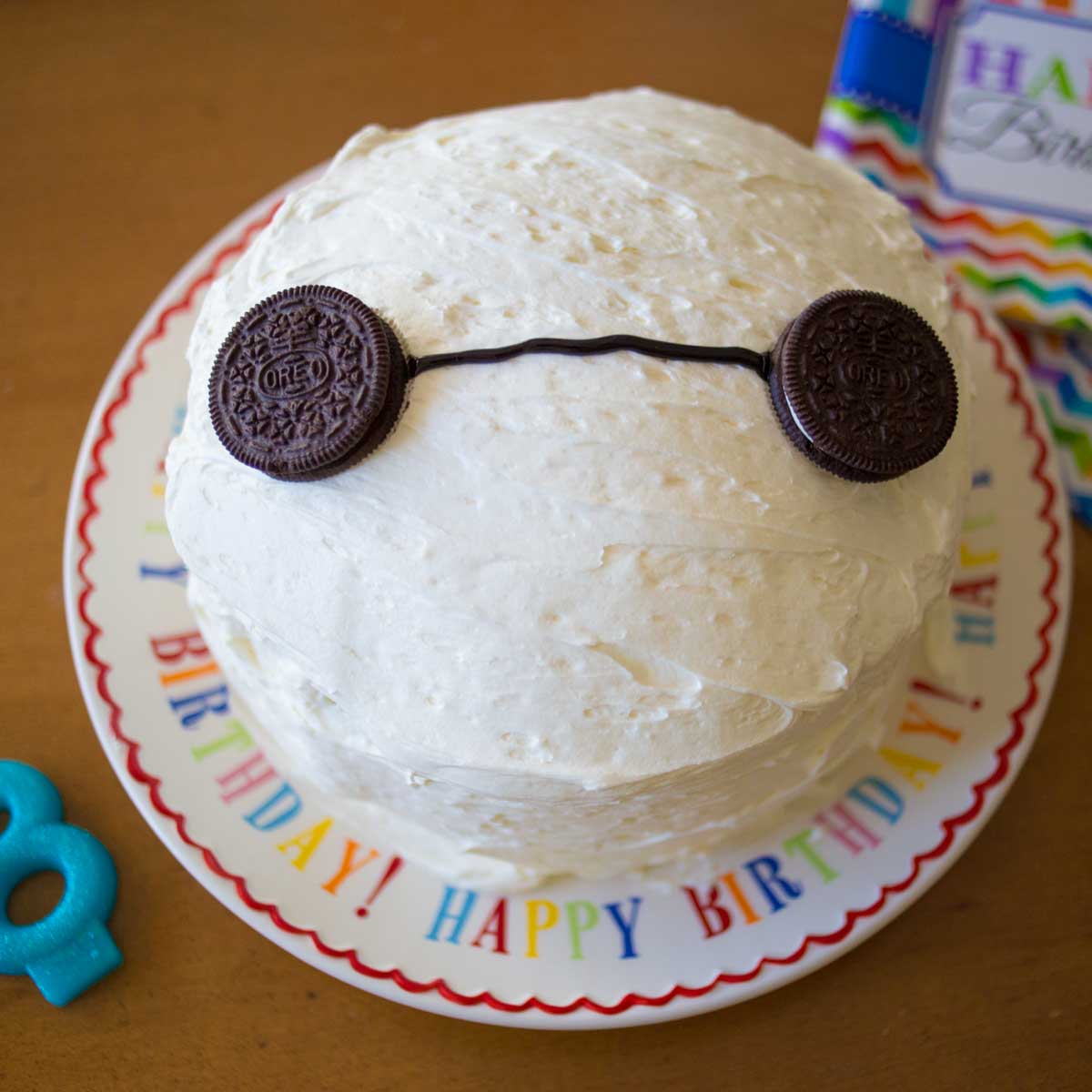 A round white-frosted layer cake has Oreo cookies for eyes to look like Baymax from Disney-Pixar's Big Hero 6.