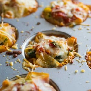 A muffin tin filled with garden lasagna cupcakes shows the spinach and tomatoes covered in melted cheese.