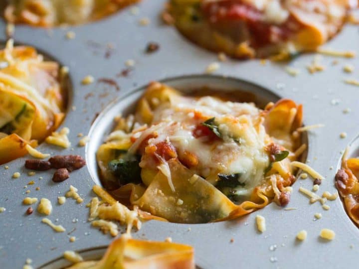 A muffin tin filled with garden lasagna cupcakes shows the spinach and tomatoes covered in melted cheese.
