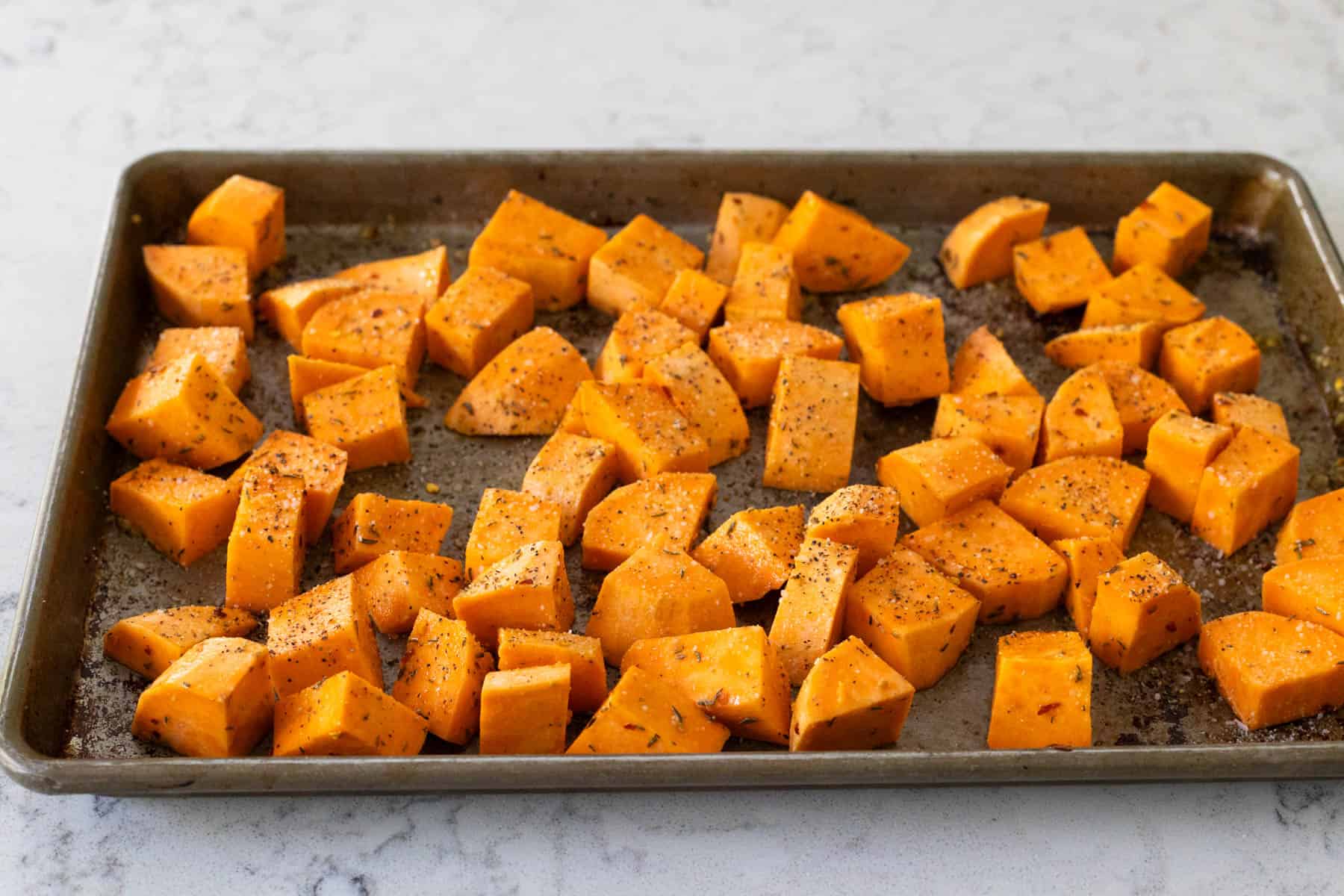 The seasoned potatoes have been spread in an even layer on a large rimmed baking sheet.
