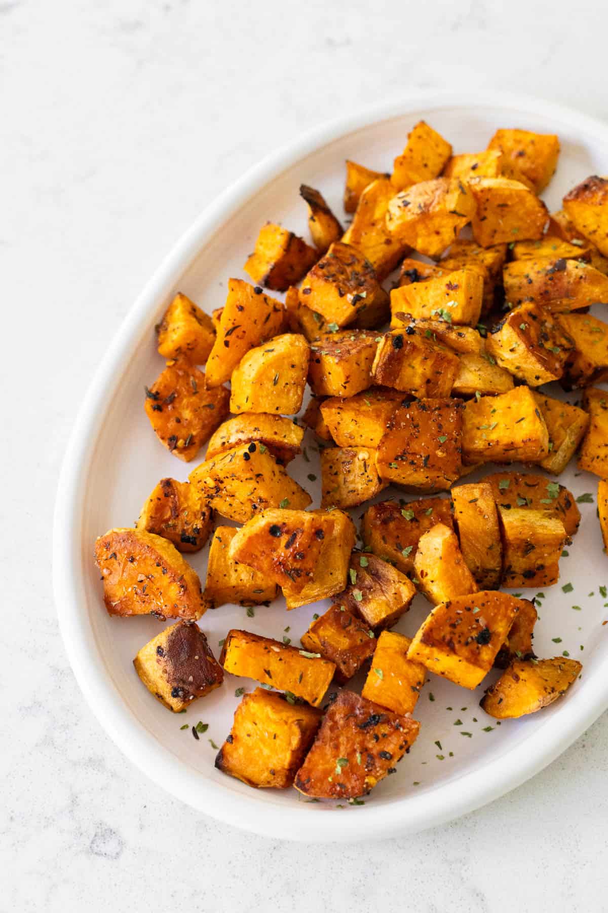 A white platter has cubed roasted sweet potatoes piled up for serving.