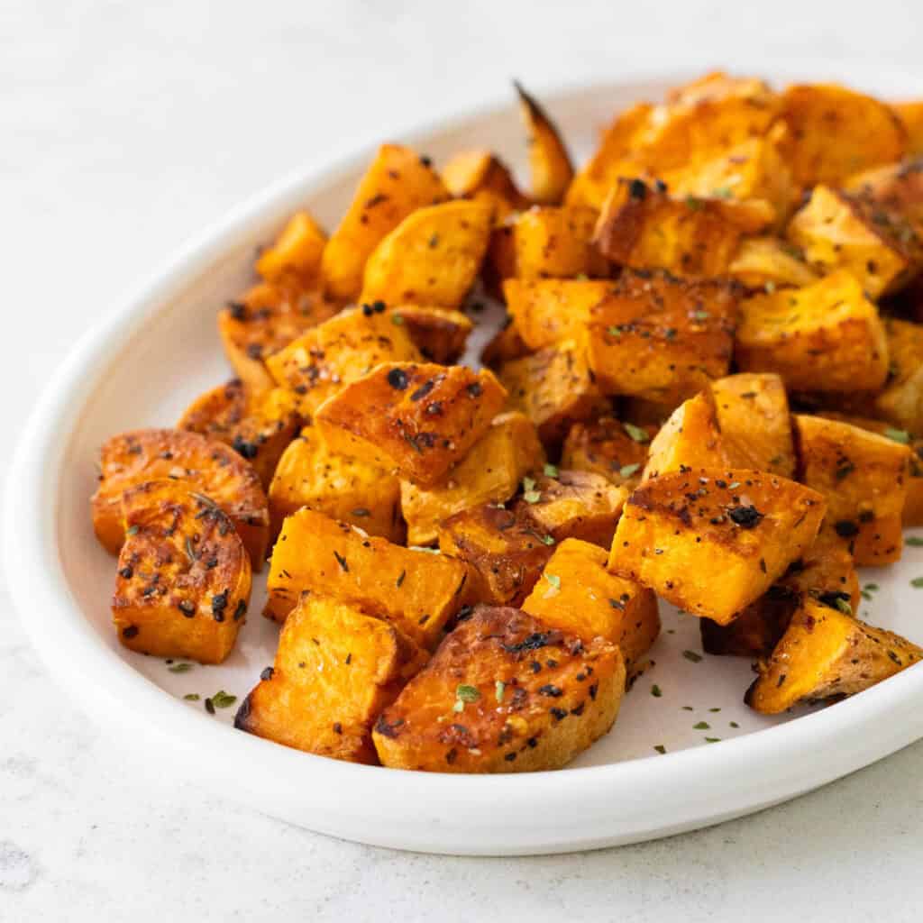 A white platter has cubed roasted sweet potatoes piled up for serving.