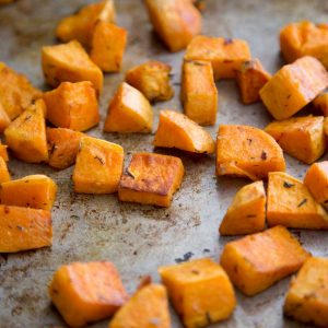 A metal baking sheet has chopped and roasted sweet potatoes scattered on it.