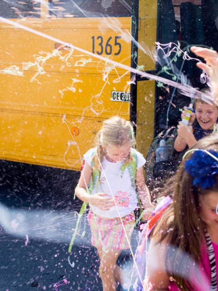 Kids coming off a school bus are getting sprayed with silly string by their parents.