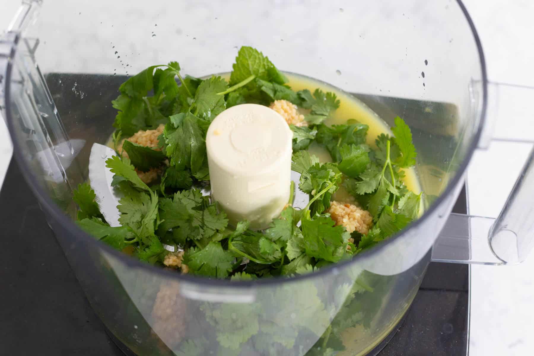 The fresh herbs and orange juice are in a food processor.