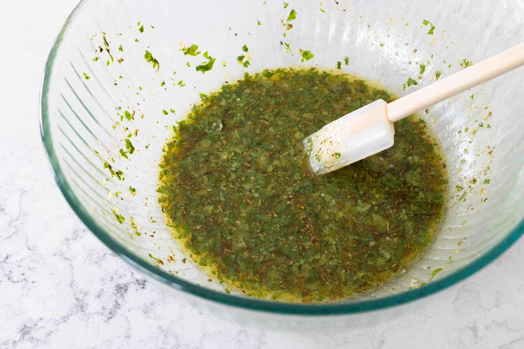 The pulsed herbs have been added to a mixing bowl and stirred together with olive oil.