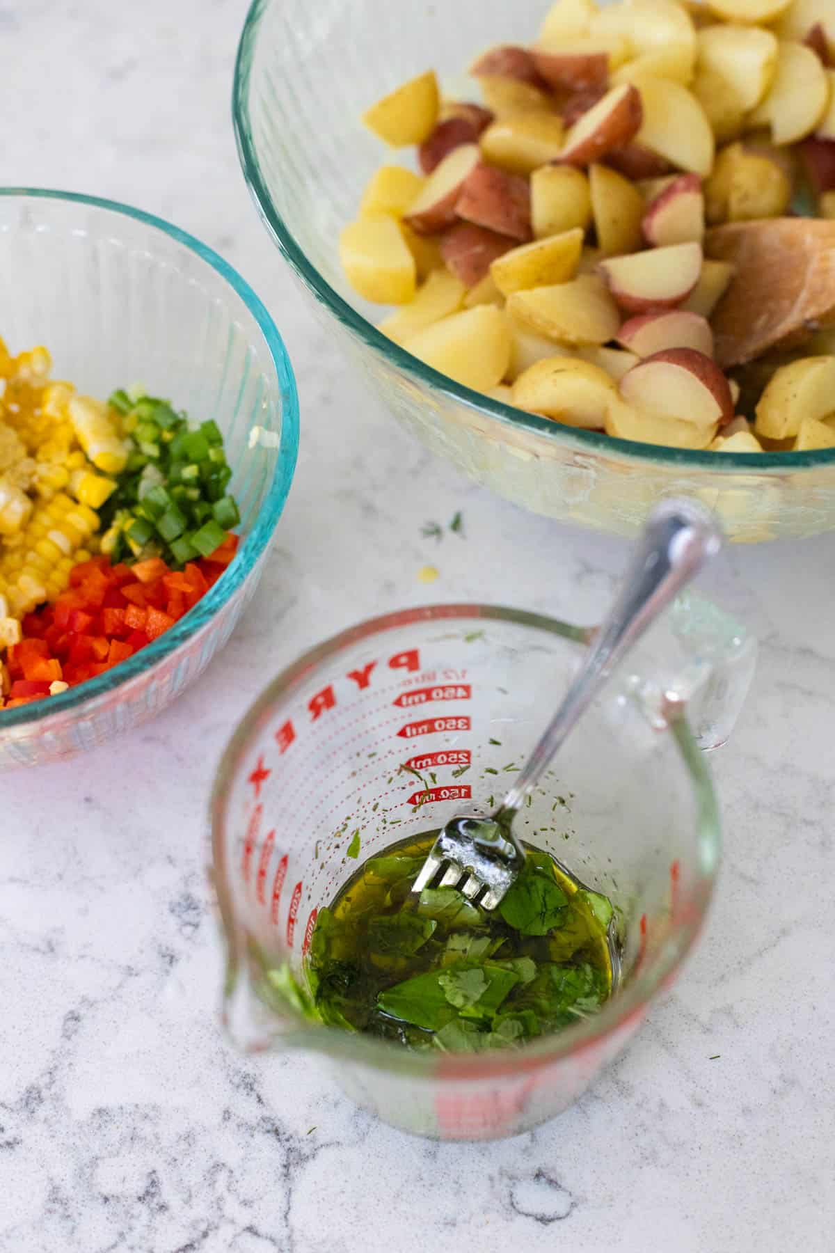The mixing bowl of veggies and a cup of vinaigrette about to be mixed with the potatoes.